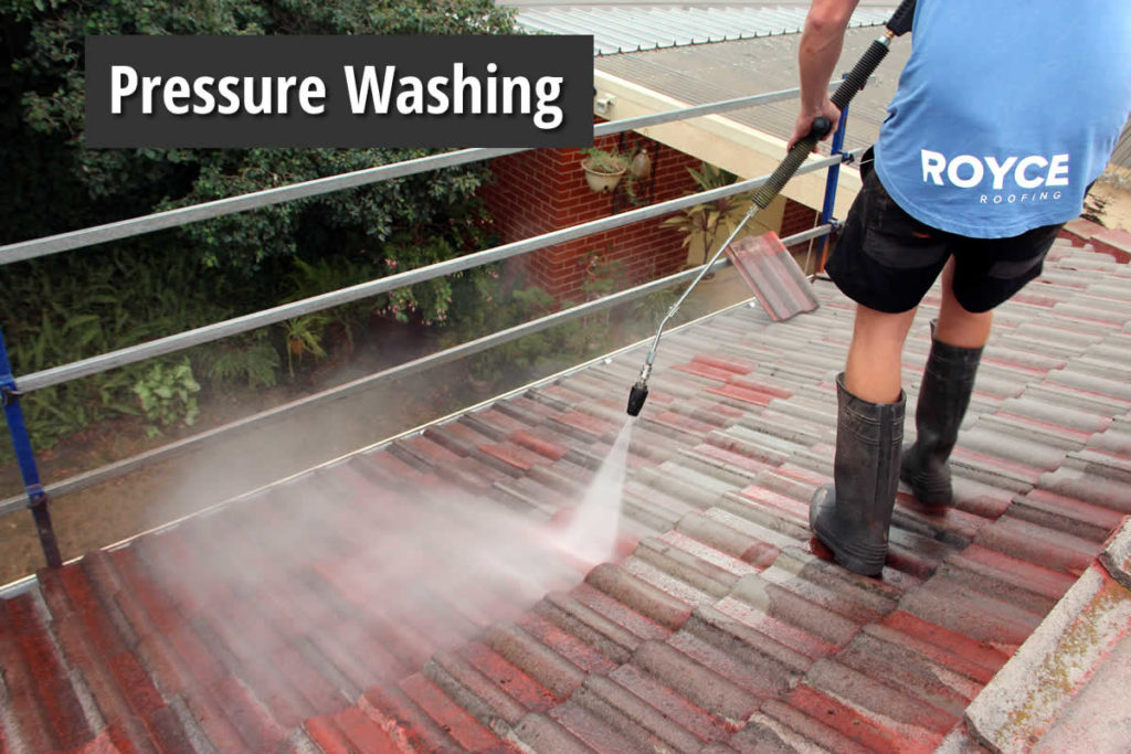 Royce Roofing crew member pressure cleaning a terracotta roof behind safety rail